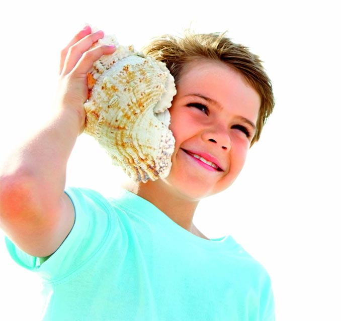 Niño escuchando una caracola de mar